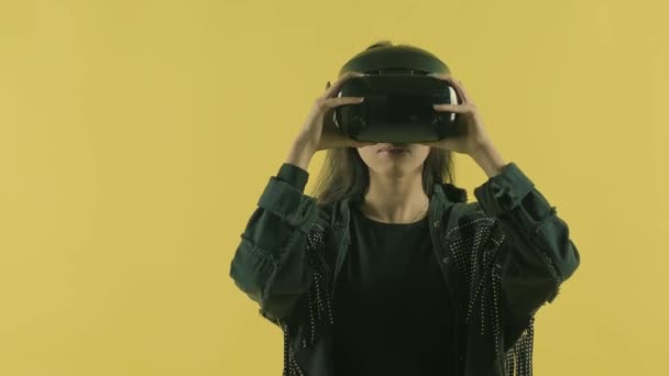 Giovane donna indossa auricolare vr, si guarda intorno e si chiede quanto sia incredibile nel mondo VR. Casco realtà virtuale sullo sfondo giallo - Filmati, video