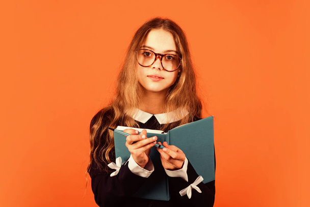 Always beautiful and smart every moment. Smart girl hold book and pen brown background. Small child with smart look in glasses. School and education. Private teaching. Smart and genius - Photo, image