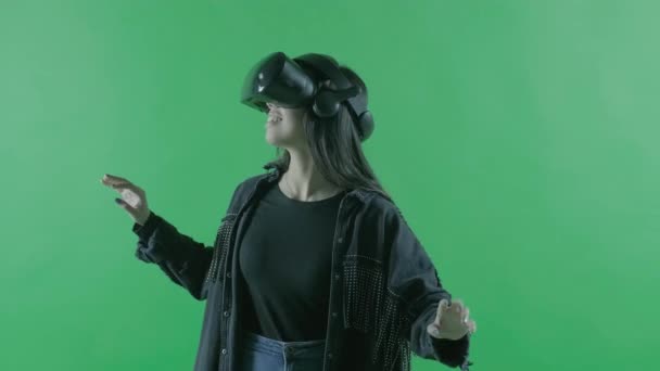 Молодая женщина смотрит вокруг и удивляется, как удивительно в VR гарнитуре. Шлем виртуальной реальности на зеленом фоне. Ключ хромы
 - Кадры, видео