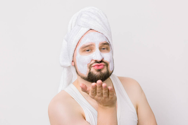 Duygusal açıdan komik bir adam sabah duş aldıktan sonra beyaz bir maske takıyor kameraya bakıyor ve hava öpücüğü veriyor. Kapalı portre, beyaz üzerinde izole - Fotoğraf, Görsel