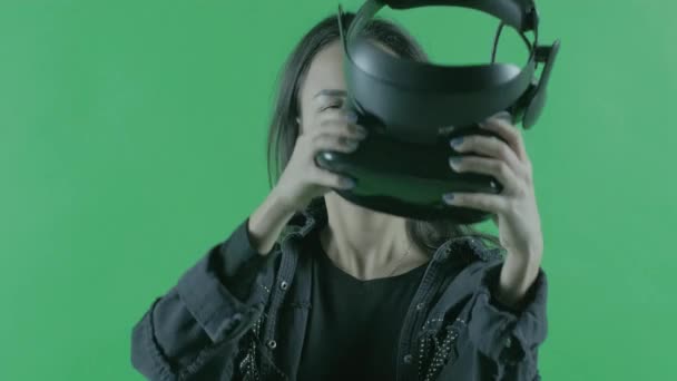 Молодая женщина надевает VR гарнитуру. Шлем виртуальной реальности на зеленом фоне. Ключ хромы
 - Кадры, видео