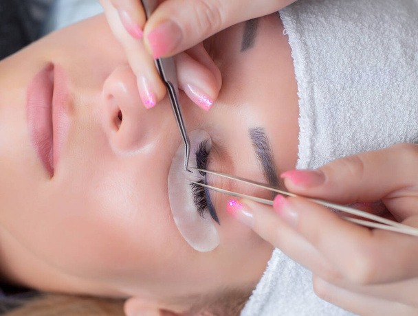 Eyelash extension procedure close up. Beautiful Woman with long lashes in a beauty salon. - Photo, Image
