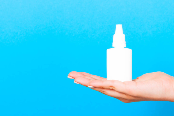 Primer plano de la mano de la mujer sosteniendo una botella de aerosol nasal en fondo azul con espacio para copiar
. - Foto, imagen