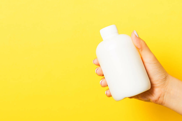 Close up of female hand holding cosmetics bottle at yellow background with copy space. - Photo, Image