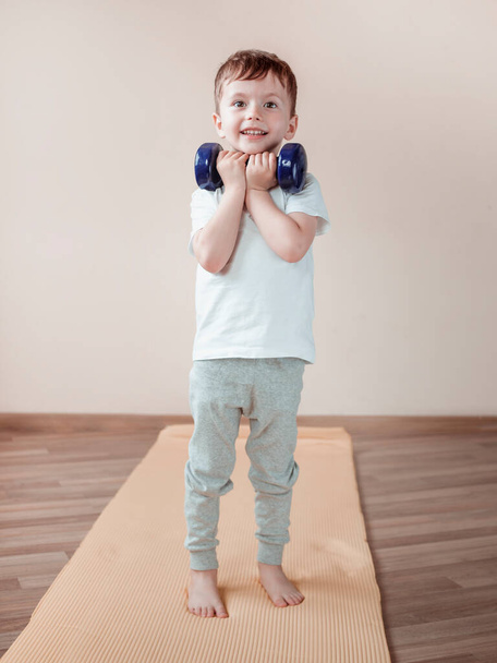 Portrait of a young boy working out with big dumbbell. Sport at home, living room interior - Photo, Image