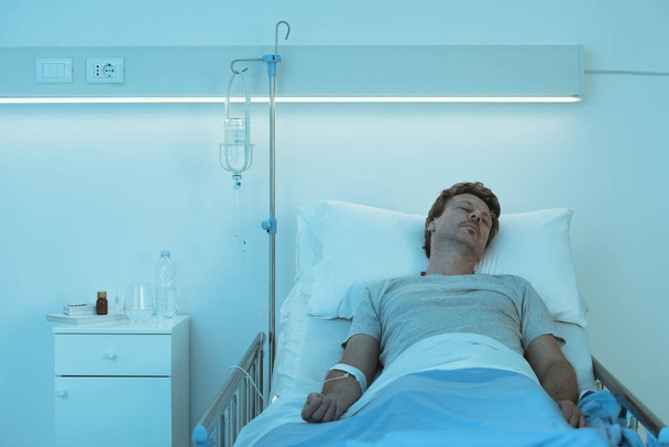 Männlicher Patient liegt im Krankenhausbett mit IV-Tropf, Medizin und Gesundheitskonzept - Foto, Bild