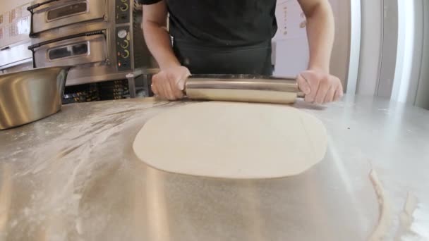 Italiaanse pizzakoks die het deeg op een met bloem bestrooide ondergrond vormen en een deeg uitrollen - Video