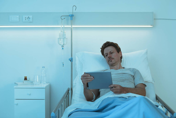 Дорослий безсонний пацієнт лежить в лікарняному ліжку вночі, він дивиться фільми зі своїм цифровим планшетом
 - Фото, зображення
