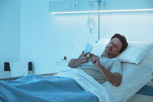 Insomnie patient inquiet couché tard dans la nuit à l'hôpital et bavarder avec son smartphone - Photo, image