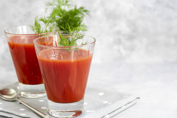 Tomato juice in glass cups. On a light gray background. Vitamin drink. Garnished with sprigs of dill. Copy space. - Photo, Image