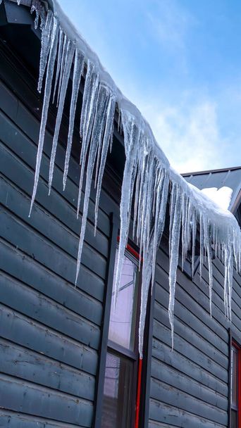 Pystysuora Sharp jääpuikot reunalla luminen koti katto taivasta ja puuta vasten talvella - Valokuva, kuva