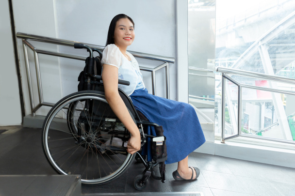 Jovem deficiente mulher em cadeira de rodas perto de deficientes passarela transporte conveniência para deficientes conceito
. - Foto, Imagem