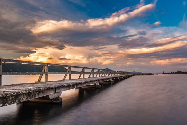 Muelle de madera viejo disparado con larga exposición durante la puesta del sol. Ubicación es Tokaanu Wharf ubicado en la región de Taupo en North Island, Nueva Zelanda
. - Foto, imagen