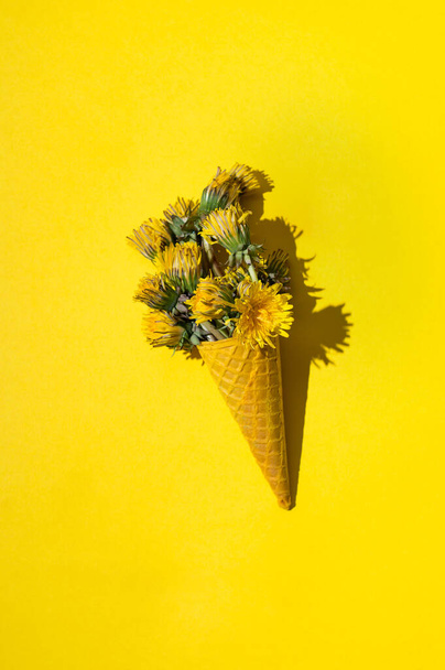waffle cone with dandelion flowers on bright yellow background - Photo, image