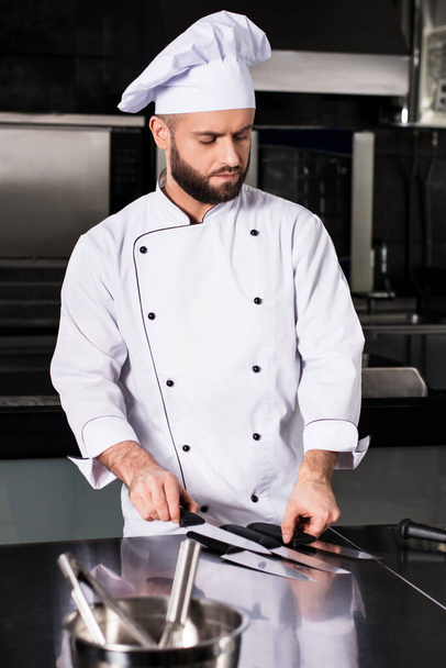 Chef male at kitchen restaurant. Concentrated male professional with knives. - Foto, Imagem