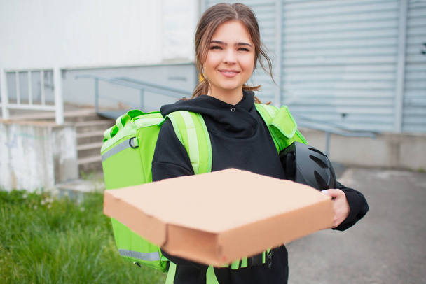 食品配送のコンセプト。ピザ配達の女性は緑の冷蔵庫のバックパックを持っています。彼女はより速く配達し、顧客に行きたいと思う。彼女は私たちに食べ物を持ってきて、彼女がどのように見えるかを. - 写真・画像