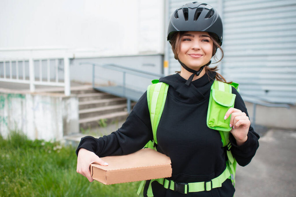 Concepto de entrega de alimentos. La repartidora de pizza tiene una mochila con nevera verde. Quiere entregar más rápido y llegar a los clientes. Nos trajo comida y nos muestra cómo se ve.
. - Foto, Imagen