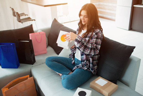 Shopping online, a young woman ordered home delivery. Now she sits on the couch and unpacks her new purchases. - Foto, imagen