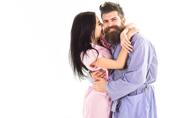 Relations goals concept. Couple in love hugging in pajama, bathrobe. Couple cuddling, girl kissing macho, isolated on white background. Couple, family on smiling faces happy in morning, copy space - Фото, зображення