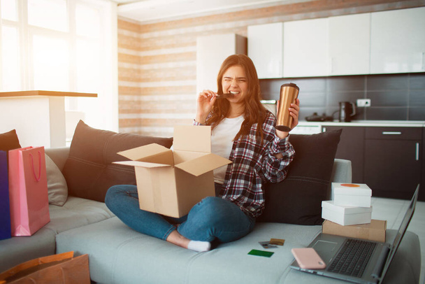 Shopping online, a young woman ordered home delivery. Now she sits on the couch and unpacks her new purchases. - Foto, Bild