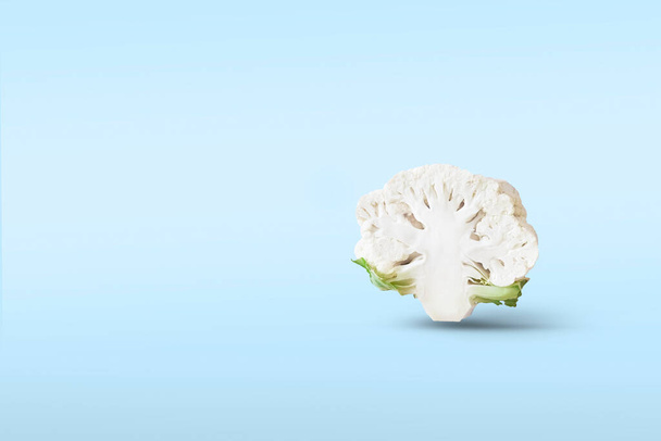 One Half a head of cut cauliflower closeup levitate in the air on a blue background with a shadow. Creative flying food concept.Minimalistic vegetable background with copy space for text. - Foto, imagen