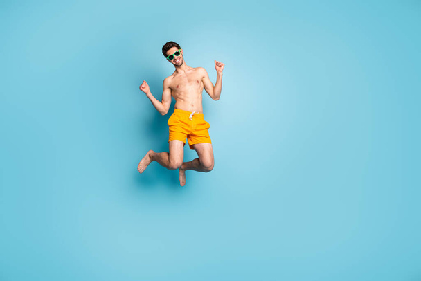 Full length body size view of his he nice attractive cheerful cheery guy in swimming shorts jumping having fun isolated on bright vivid shine vibrant green blue turquoise color background - Fotó, kép