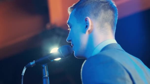 Człowiek śpiewający piosenkę w mikrofonie podczas występu na scenie na koncercie rockowym. Close up man gwiazda rocka piosenkarka na koncert muzyczny na kolorowym tle światła - Materiał filmowy, wideo