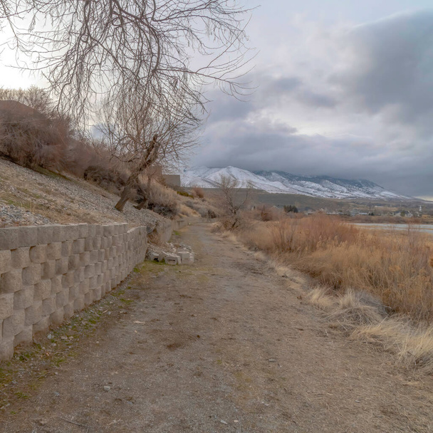 Square Dirt road along the retaining wall of slope overlooking lake and snowy mountain - Photo, Image
