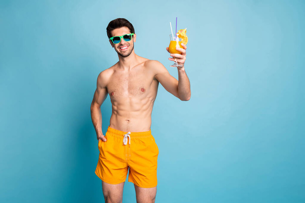 Photo of cheerful positive handsome man smiling toothily with hand in pocket wearing yellow shorts isolated pastel blue color background - Zdjęcie, obraz