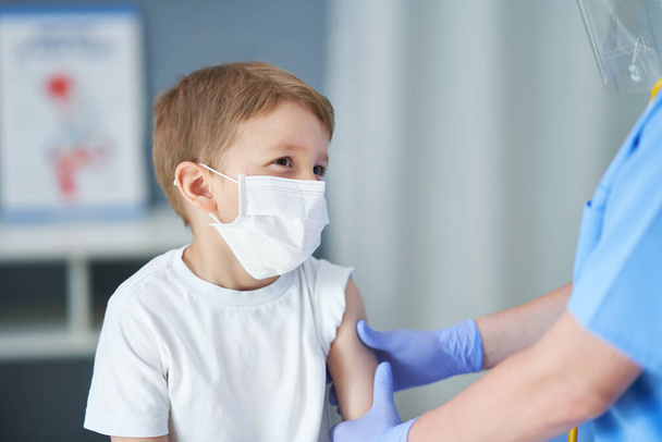 Πορτρέτο του αξιολάτρευτου μικρού αγοριού που εμβολιάζεται στο ιατρείο - Φωτογραφία, εικόνα