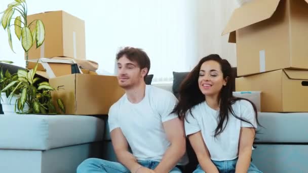 Young couple move into new apartment. Man and woman sit together on floor and dance at same time. Have fun together in new apartment. Cheerful positive people on video. - Footage, Video
