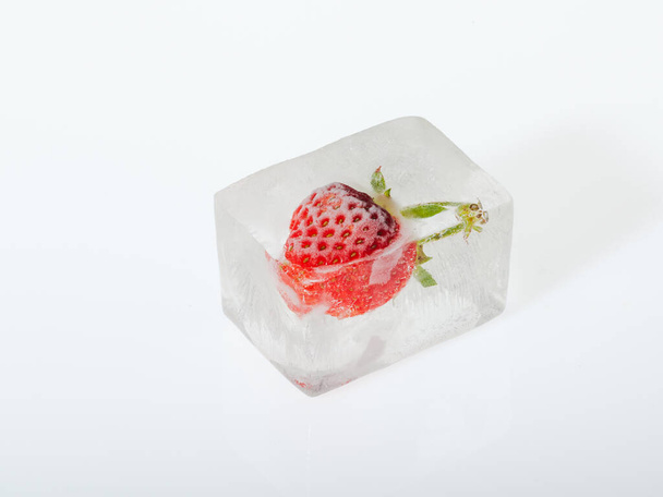 Strawberry frozen in the ice on white background closeup. Concept of freezing fruits. - Photo, Image