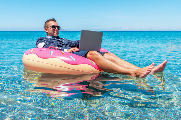Businessman using laptop computer on an inflatable donut in the sea. Summer vacation concept. - Photo, image