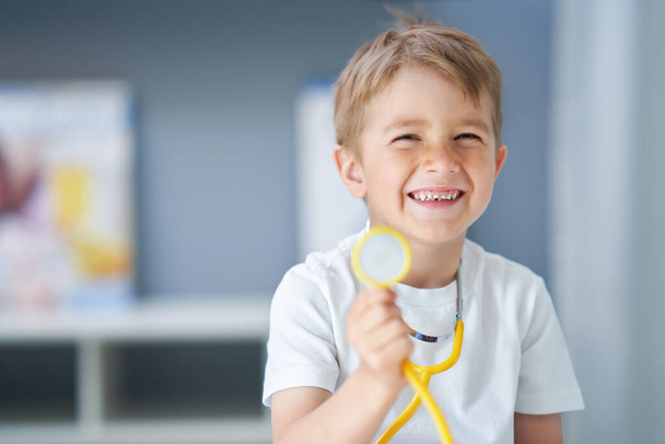 Mały lekarz ze stetoskopem uśmiechnięty w gabinecie lekarskim - Zdjęcie, obraz