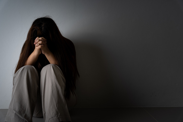 Smutna kobieta przytula kolano i płacze samotnie w ciemnym pokoju. Depresja, nieszczęśliwy, zestresowany i zaburzenia lękowe pojęcie. - Zdjęcie, obraz