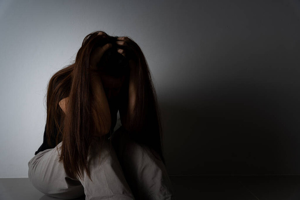 trieste vrouw omhelst haar knie en huilt alleen in een donkere kamer. Depressie, ongelukkig, gestresst en angststoornis concept. - Foto, afbeelding