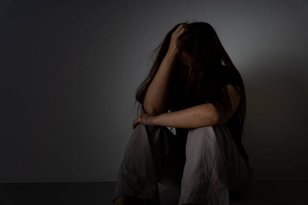 Surullinen nainen halaa polveaan ja itkee yksin pimeässä huoneessa. Masennus, onneton, stressaantunut ja ahdistuneisuushäiriö käsite
. - Valokuva, kuva