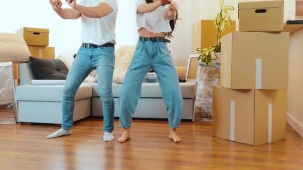 Young couple move into new apartment. Low view of man and woman stand barefeet on floor in room and dancing together. Relaxing and resting during relocation. - Filmati, video