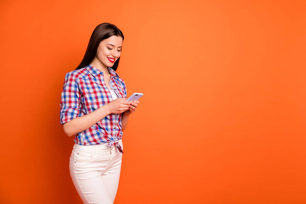 Turned photo of positive girl having rest relax stand copyspace use cell phone read social media blog news post comment feedback wear plaid outfit isolated over orange color background - Φωτογραφία, εικόνα
