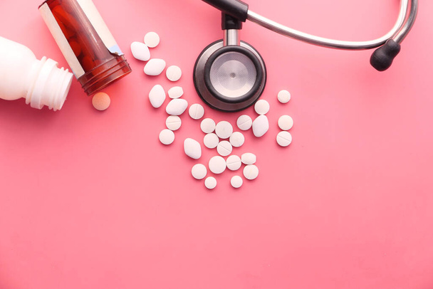 pillen, stethoscoop en container op roze achtergrond  - Foto, afbeelding