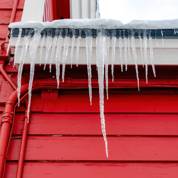 Square Spiked jäädytetty jääpuikot katolla kodin elinvoimainen punainen puinen ulkoseinä - Valokuva, kuva