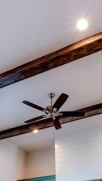 Vertical Ceiling fan with lights flanked by decorative wood beams and recessed lighting - Photo, Image