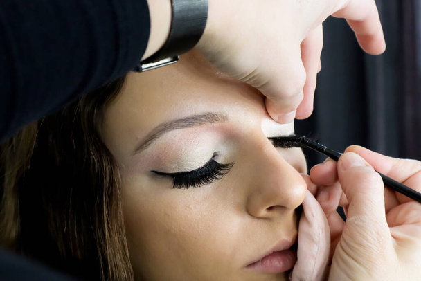 close up of make-up artist applying liquid eyeliner on model's eyes, customer with cotton pads on face getting professional make up - Fotoğraf, Görsel