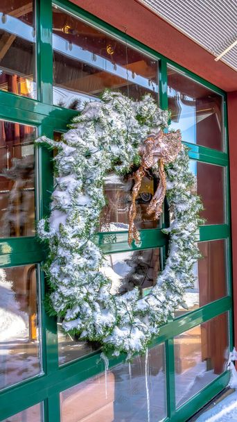 Вертикальная рама Замороженный венок на стеклянной стене здания, который отражает зимний пейзаж
 - Фото, изображение