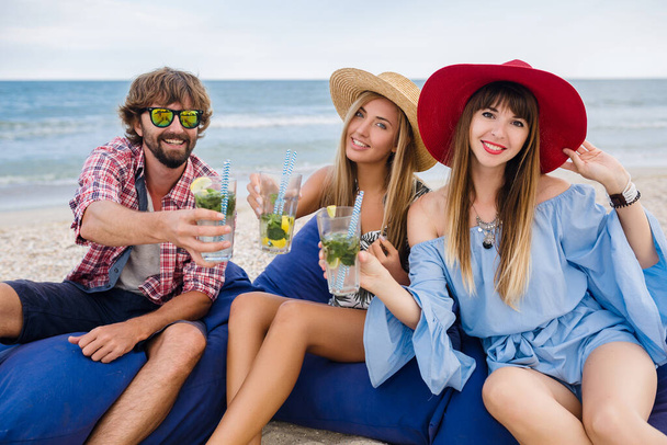 young hipster company of friends on vacation at beach cafe, drinking mojito cocktail, happy positive, summer style, smiling happy, two women and man having fun together, talking, flirt, romance, three - Photo, Image