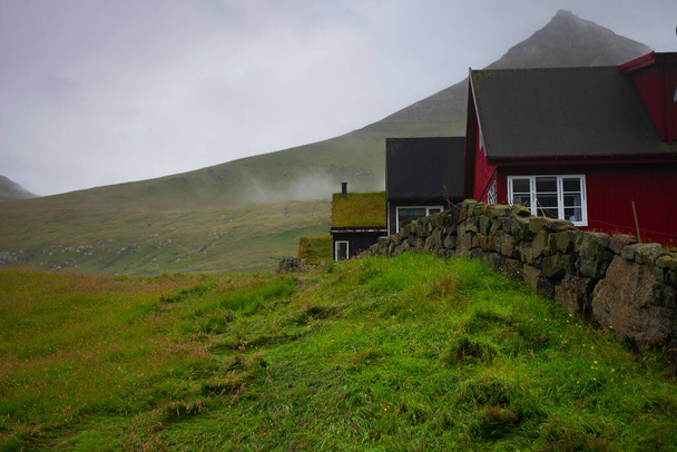 Casas coloridas típicas das Ilhas Faroé com grama em torno de um dia nebuloso atrás de uma cerca
 - Foto, Imagem