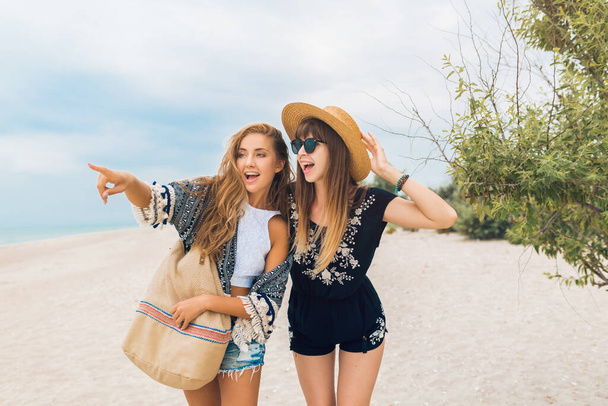 stylish pretty women on summer vacation on tropical beach, bohemian style, friends together, fashion accessories, smiling, happy emotion, positive mood, pointing finger, traveling tourists - Foto, Imagen