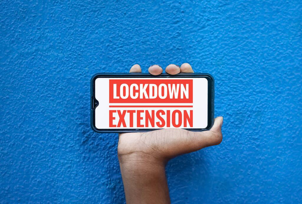 Lock Down Extension word on mobile screen isolated on blue background with copy space for text. Person holding mobile on his hand and showing front of the screen wording Lock Down Extension. - Photo, Image