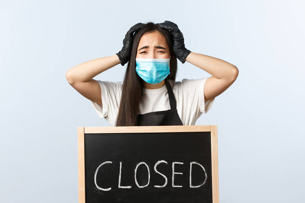 Μικρές επιχειρήσεις, πανδημία covid-19, πρόληψη του ιού και των εργαζομένων έννοια. Ιδιοκτήτης καφετέριας με ιατρική μάσκα πανικοβάλλεται καθώς η επιχείρηση κλείνει, στέκεται κοντά σε κλειστή πινακίδα - Φωτογραφία, εικόνα