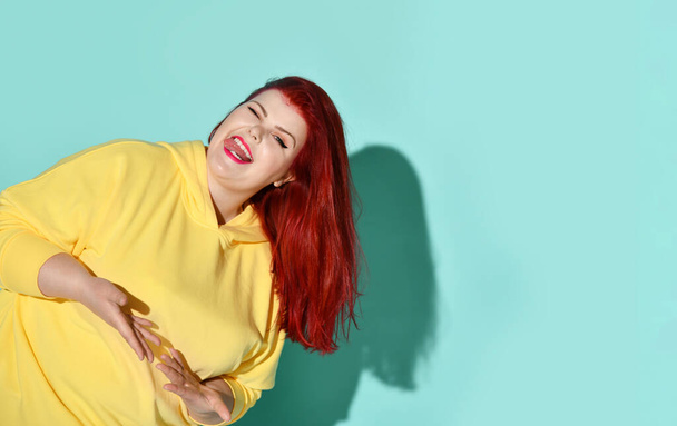 Chubby young woman with red hair holding both hands close to chest with palms up asking to make a choice. Cropped studio shot isolated on blue - Foto, Bild